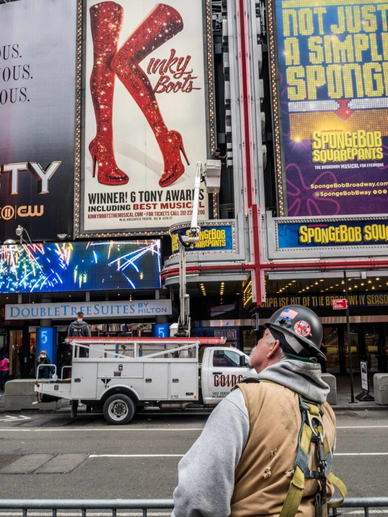 A construction worker standing in New York's Times Square contemplates a large billboard of the Broadway Show, Kinky Boots